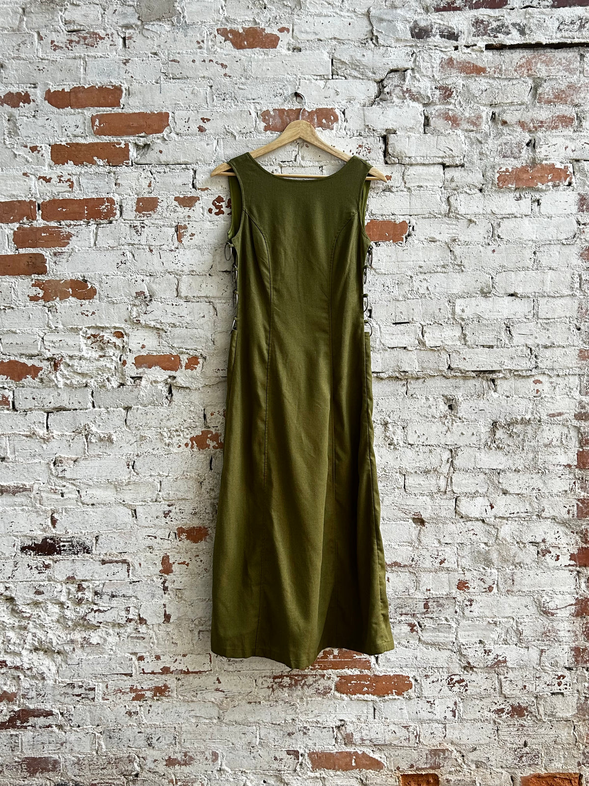 Green dress hanging on a wooden hanger against a textured brick wall.