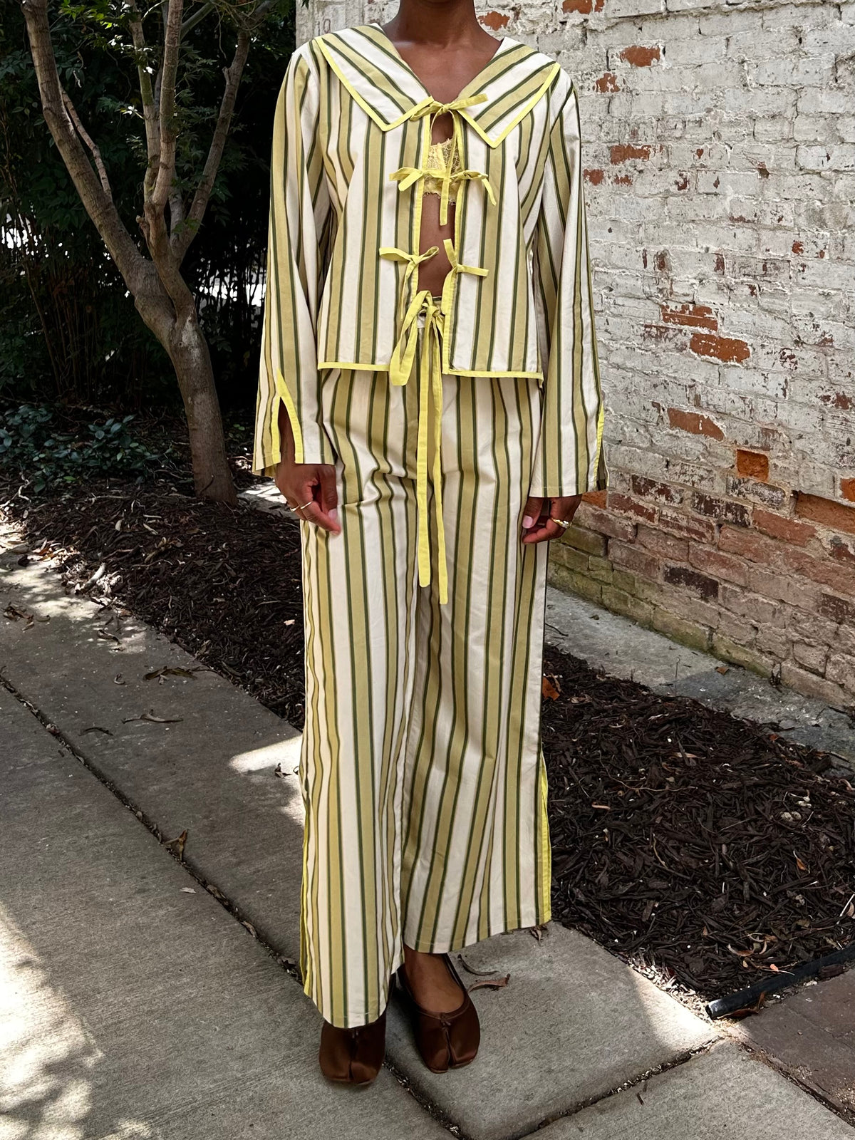 Person wearing a striped outfit with yellow accents against a brick wall.