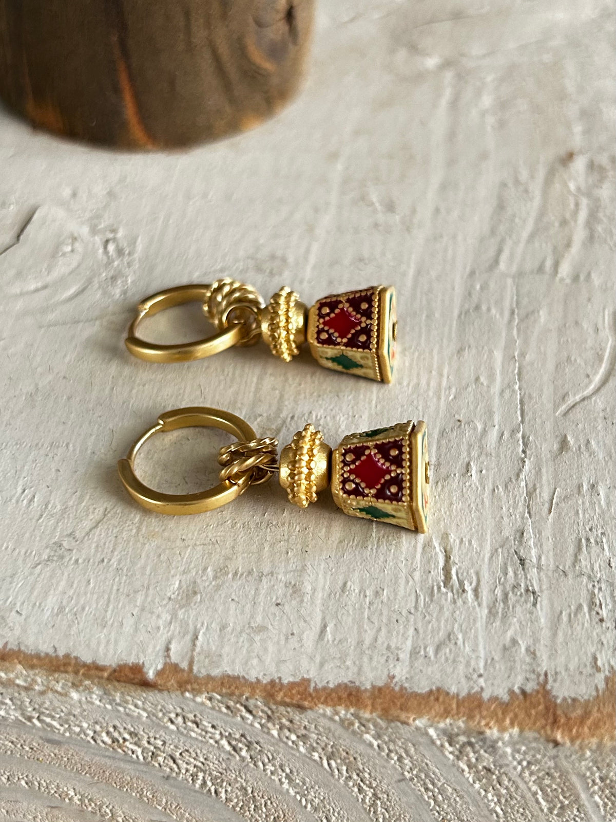 Gold bell-tower-shaped earrings with red and green accents on a textured white surface.