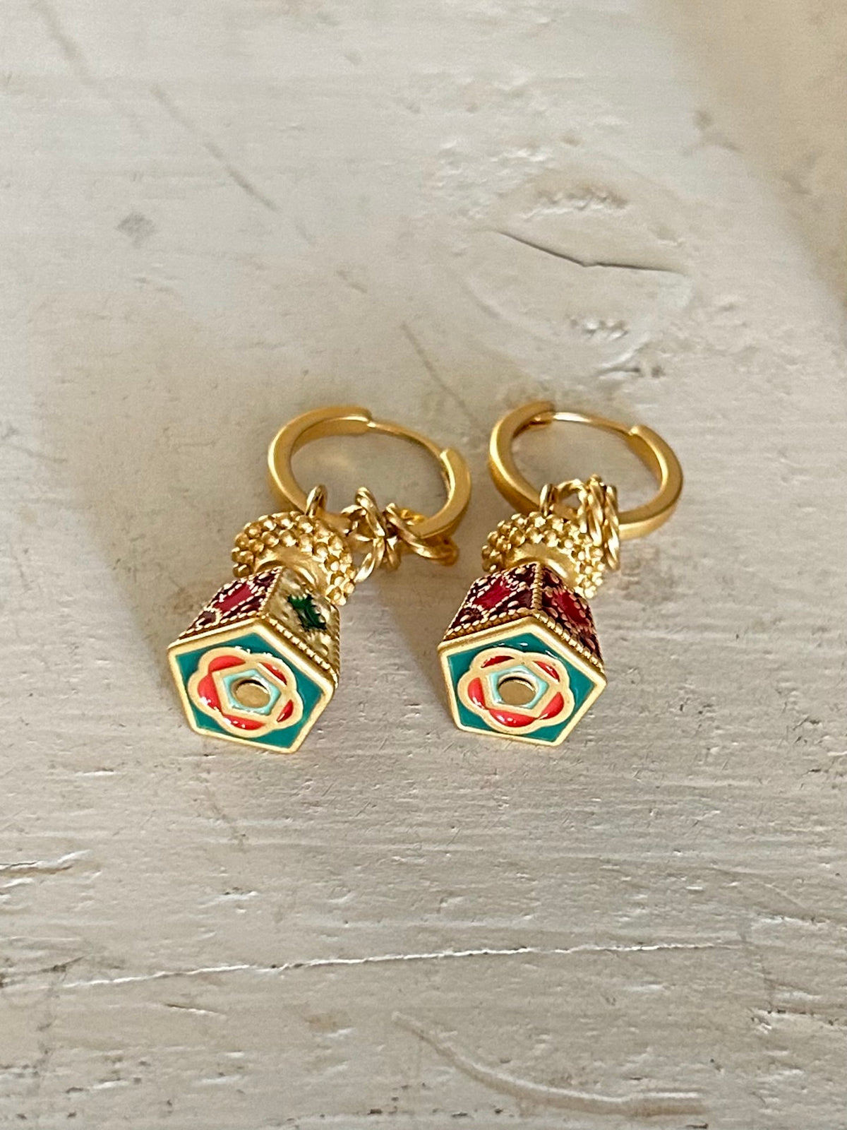 Gold earrings with colorful hexagonal charms on a light wooden surface