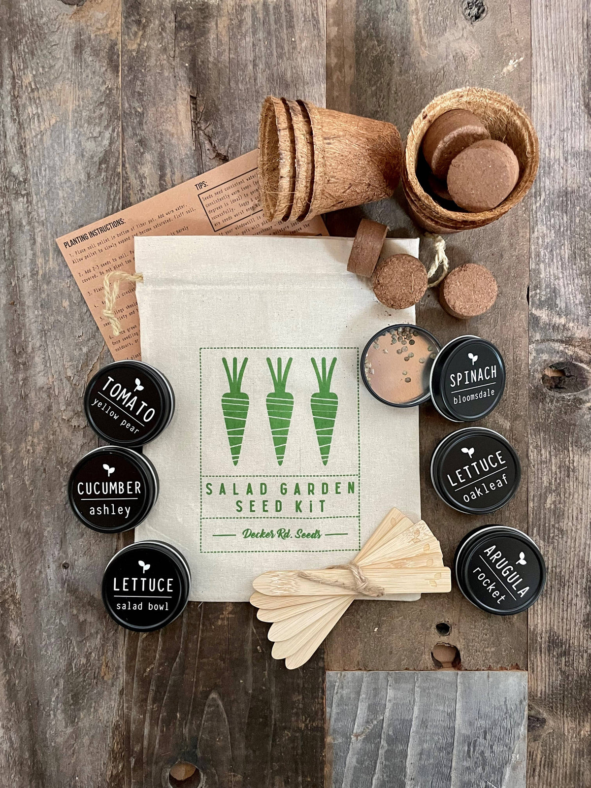 Salad garden seed kit with seed packets and wooden tools on a wooden surface