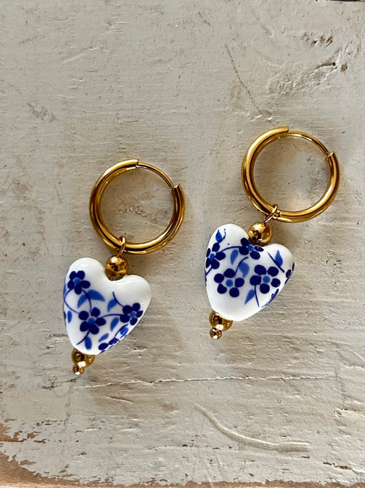Pair of gold hoop earrings with blue and white heart-shaped charms on a textured surface.