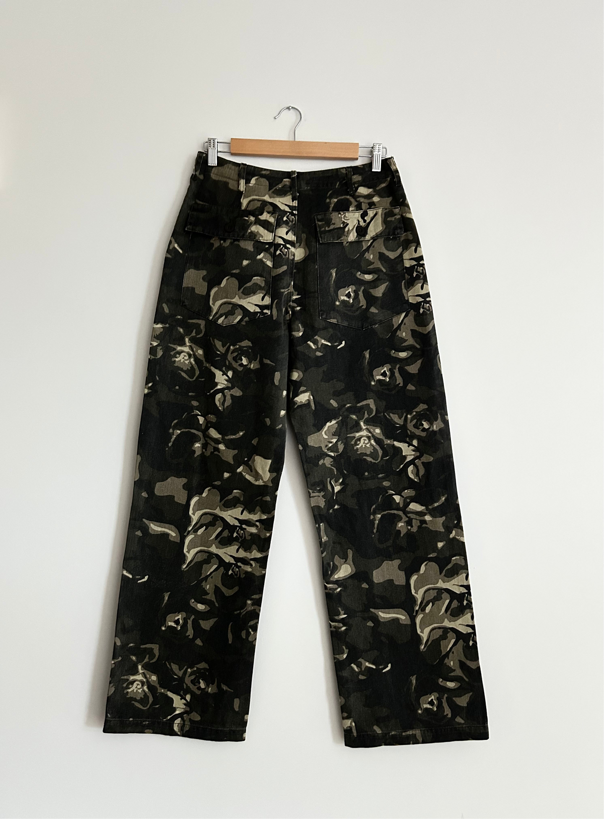 Camouflage-patterned pants on a hanger against a white background