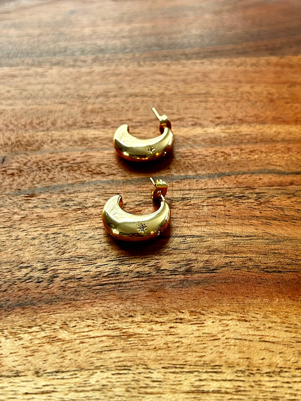 Gold crescent moon earrings on a wooden surface