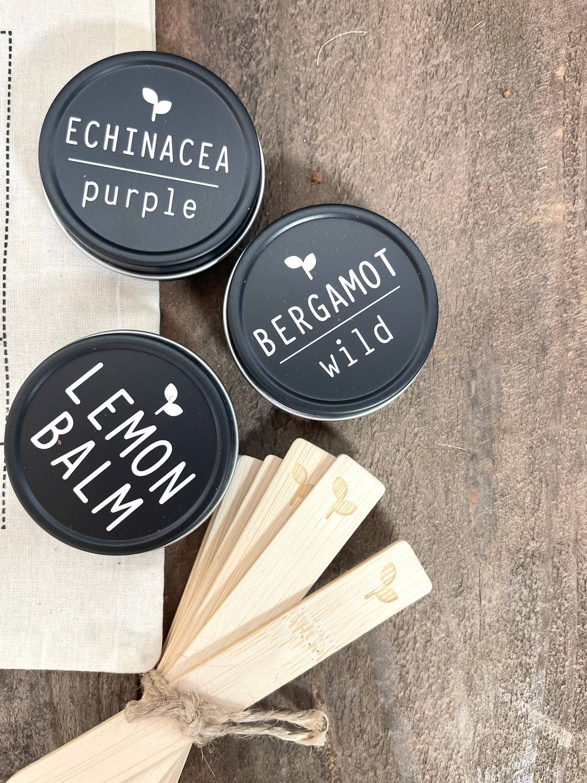 Three tins labeled 'Echinacea purple', 'Bergamot wild', and 'Lemon balm' on a wooden surface.