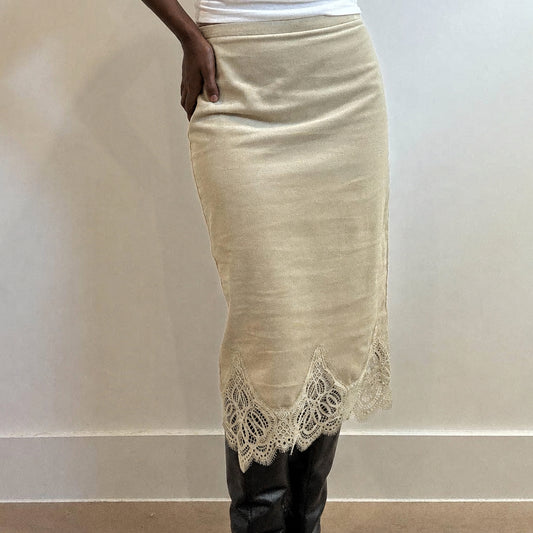 A person wearing a beige knit midi skirt with a scalloped lace hem, paired with black knee-high boots against a plain indoor wall.
