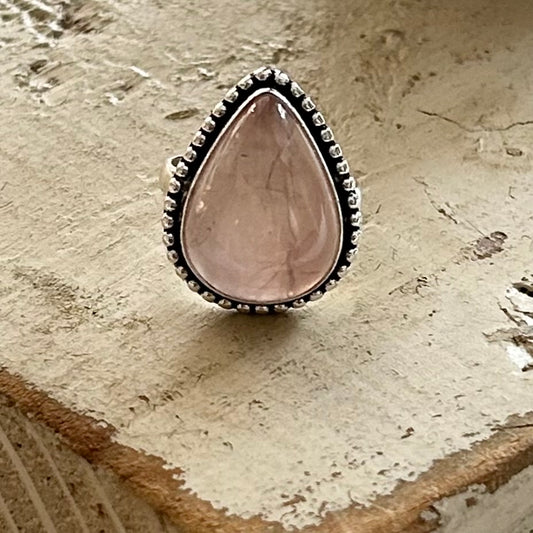 An oxidized sterling silver teardrop ring with a rose quartz stone, featuring a textured design on the metal.