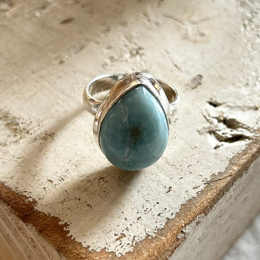 A sterling silver ring with a large teardrop-shaped Larimar gemstone set on a textured wooden surface.