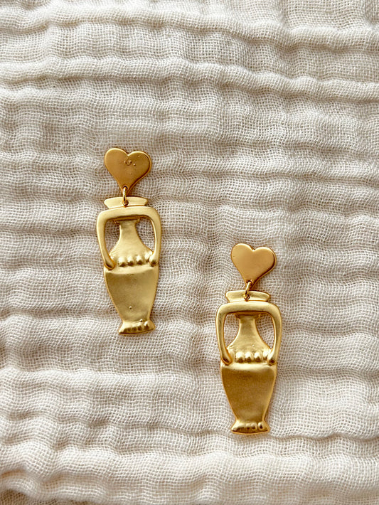 Gold urn-shaped earrings with heart details on a textured beige fabric background

Designed in California

Textured finish unique to each piece

18K Gold Plating Brass&nbsp;

Measurement (L x W inch): 1.5 x 0.5)

Nickel-free, Lead-safe