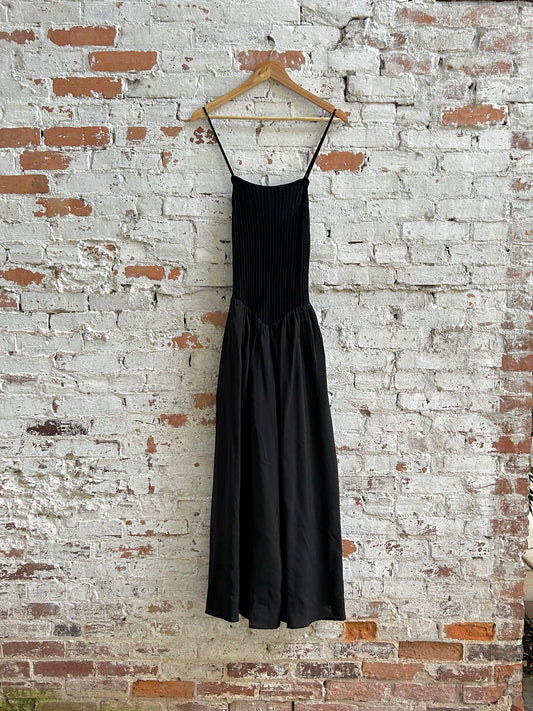 Dual textured black dress hanging on a wooden hanger against a brick wall.
