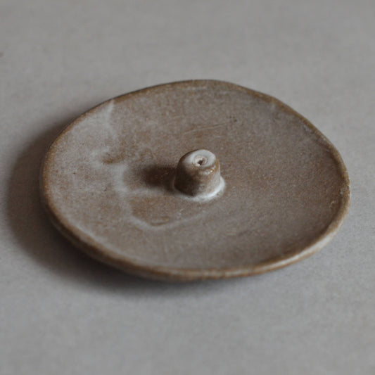 A grey brown natural colored handmade ceramic incense holder with an organic shape and a glazed finish.