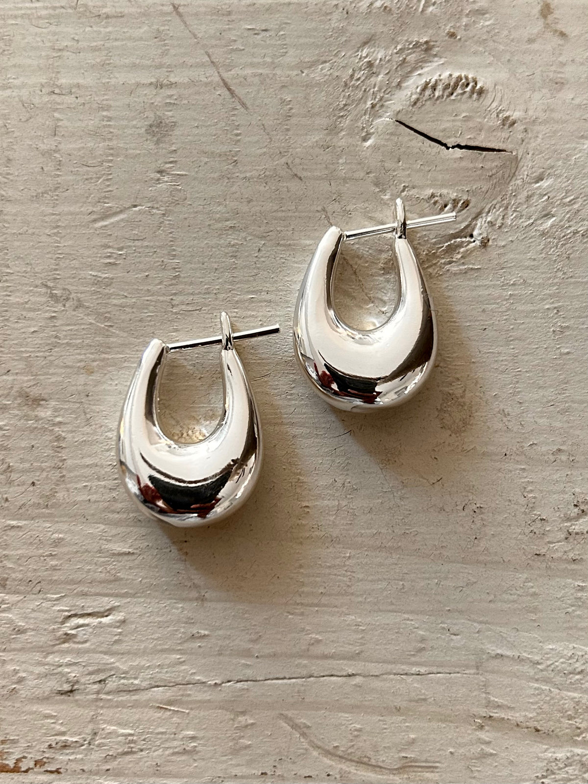 Pair of silver hoop earrings on a textured beige surface Available in Chrome/Silver and Gold Brass (gold plated)