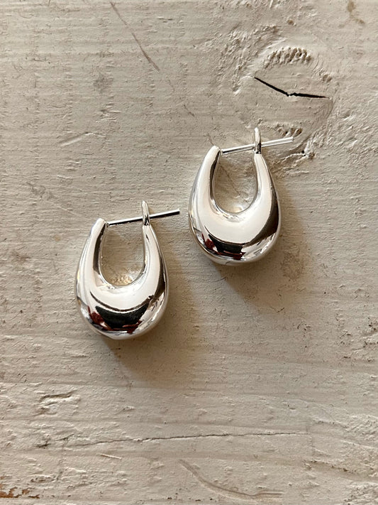 Pair of silver hoop earrings on a textured beige surface Available in Chrome/Silver and Gold Brass (gold plated)
